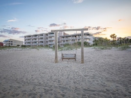 A beach with a wooden swing set and a multi-story building in the background.