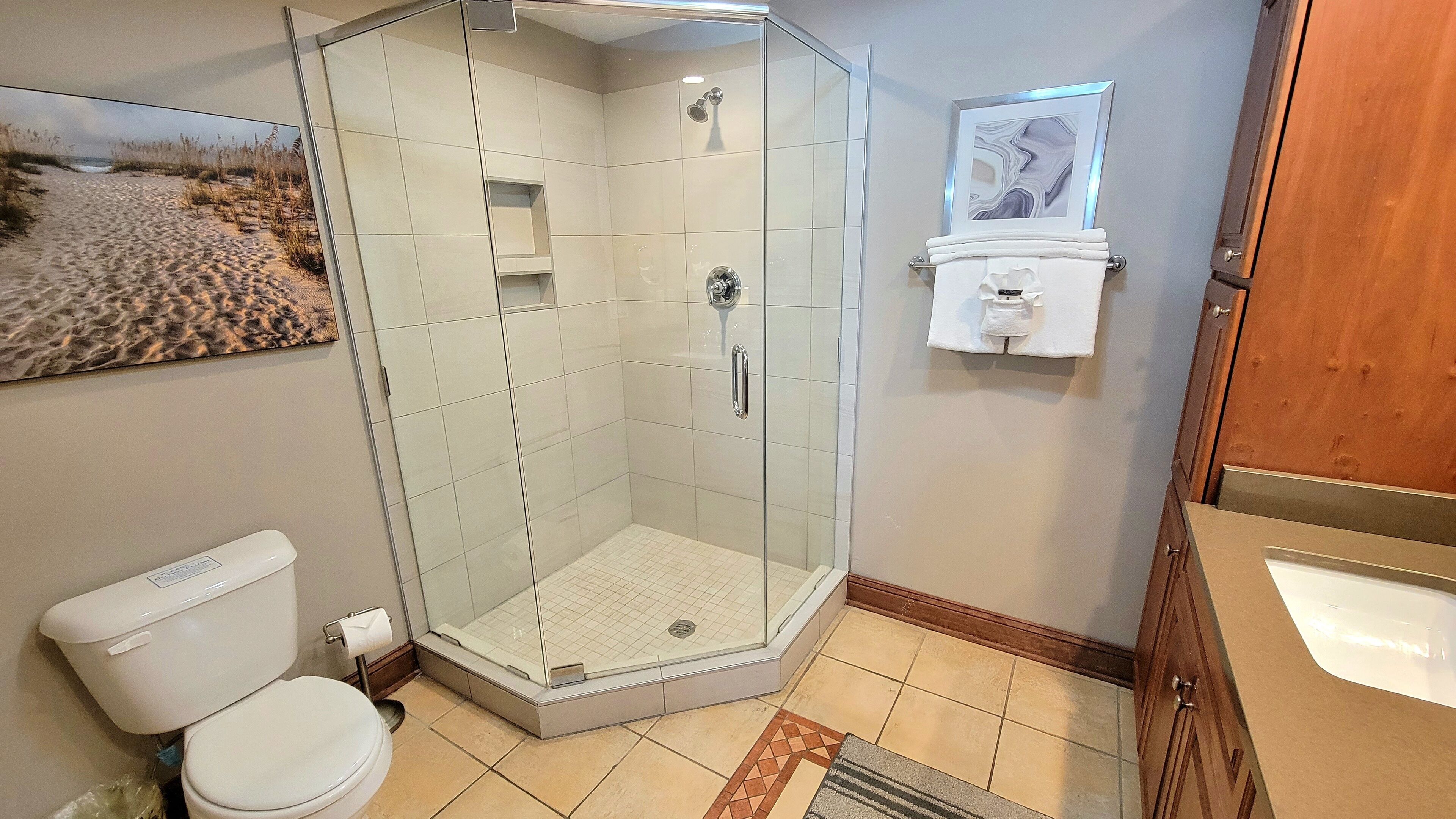 A bathroom with a glass-enclosed shower, a toilet, a sink, and a framed picture on the wall.