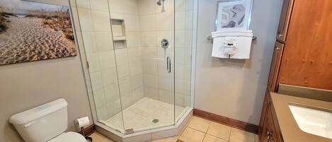 A bathroom with a glass-enclosed shower, a toilet, a sink, and a framed picture on the wall.