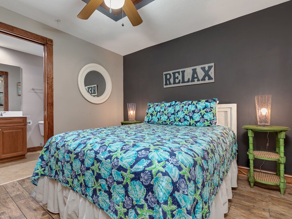 A bedroom with a bed, a mirror, a wall-mounted sign that says "RELAX", and a green side table with a lamp.