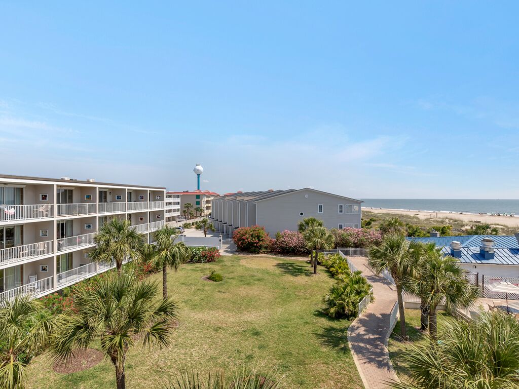 A beachfront hotel with multiple balconies, a grassy lawn, and a view of the beach.