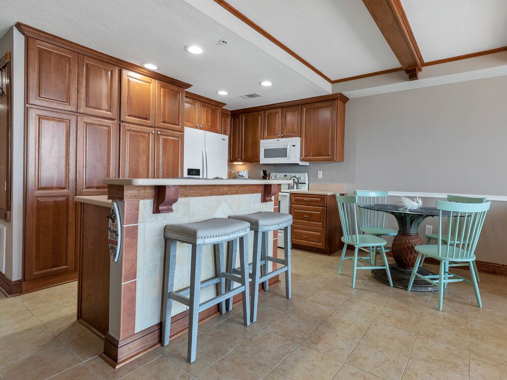 A kitchen with wooden cabinets, a microwave, a refrigerator, and a bar area with stools.