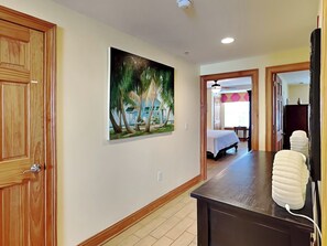 Une chambre d’hôtel avec une porte en bois, un tableau représentant des palmiers, un lit et un bureau avec un téléphone.