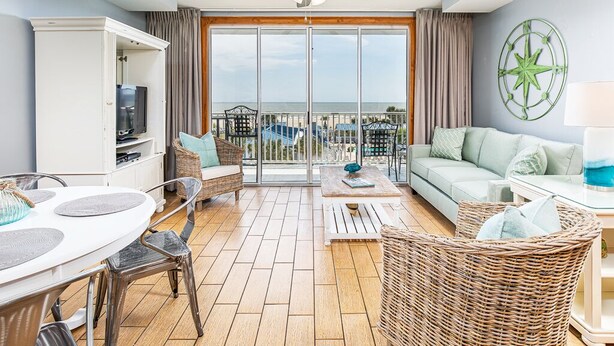 Een ruime woonkamer met balkon, plafondventilator, televisie en een rieten fauteuil.