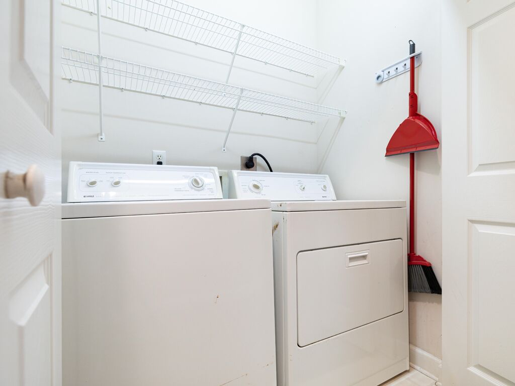 Un espace buanderie comprenant deux machines à laver blanches, une serpillière rouge et un mur blanc avec une étagère en métal.