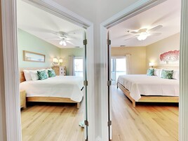 A mirrored room with two beds, ceiling fans, and a balcony with a view.