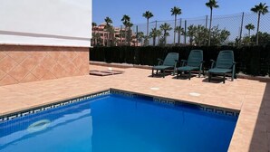 A swimming pool with a tiled deck, surrounded by a fence and palm trees. - PUSHE Village Playa Granada Beach & Golf 3 (Motril)