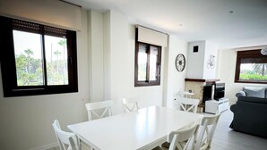 A modern living room with a white dining table and chairs, a grey sofa, and a TV. - PUSHE Village Playa Granada Beach & Golf 3 (Motril)