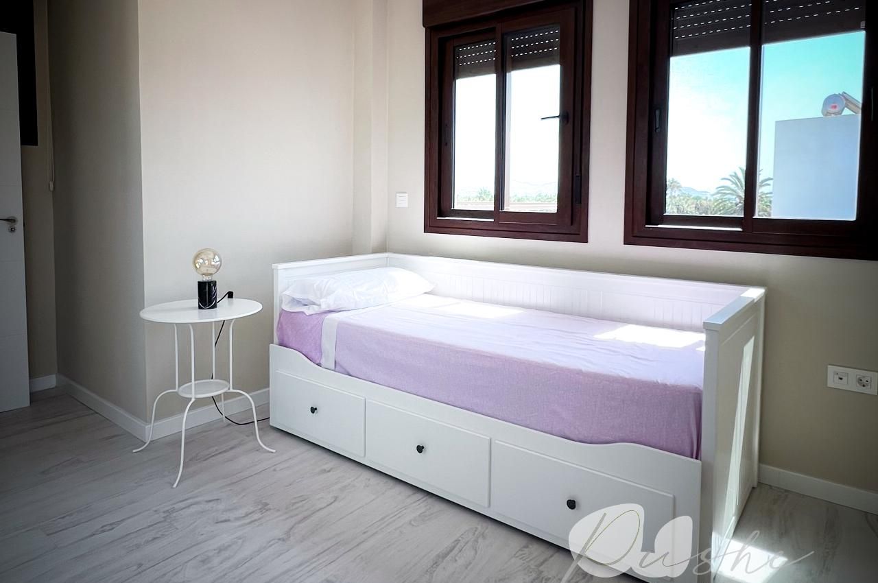 A bedroom with a single bed, a small white table, and a window with blinds.