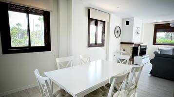 Ein modernes Wohnzimmer mit einem weißen Esstisch und Stühlen, einem grauen Sofa und einem Fernseher.