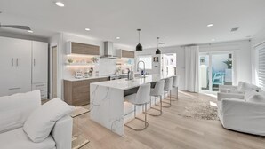 A modern kitchen with a marble island, bar stools, and pendant lighting. - Gulf Front With Private Pool- Emerald View on 30A by Royal Destinations (Santa Rosa Beach)