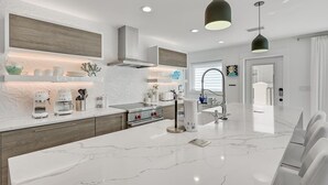 A modern kitchen with a marble island, built-in appliances, and pendant lighting. - Gulf Front With Private Pool- Emerald View on 30A by Royal Destinations (Santa Rosa Beach)