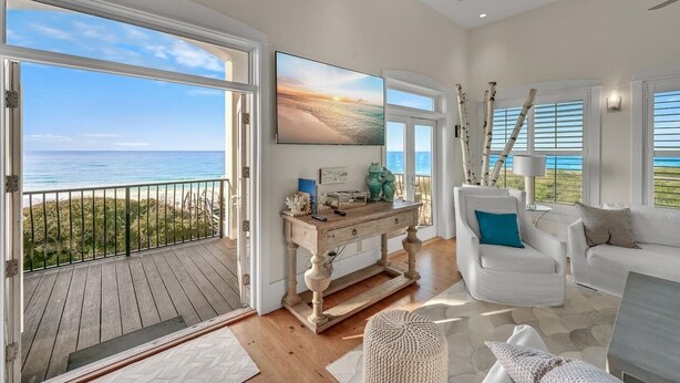 A spacious living room with a large window overlooking the ocean, a wooden console table, white furniture, and a view of the beach. - Gulf Front With Private Pool- Emerald View on 30A by Royal Destinations (Santa Rosa Beach)
