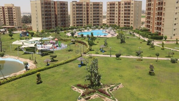 A residential complex with multiple high-rise buildings, a central swimming pool, and well-maintained green spaces. - Marseilia Land (El Alamein)
