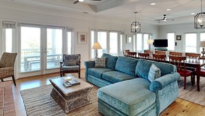 A spacious living room with a sectional sofa, a dining area with a wooden table and chairs, and large windows providing natural light. - 5 Oclock Somewhere by Tybee Vacation Rentals (Tybee Island)