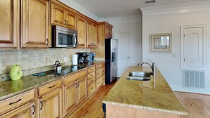 A kitchen with wooden cabinets, a stainless steel sink, a microwave, and a refrigerator. - 5 Oclock Somewhere by Tybee Vacation Rentals (Tybee Island)