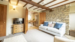 A cozy living room with a white sofa, a television on a wooden stand, and a stone wall. - Fairview, Ampleforth, North York Moors (Ampleforth)