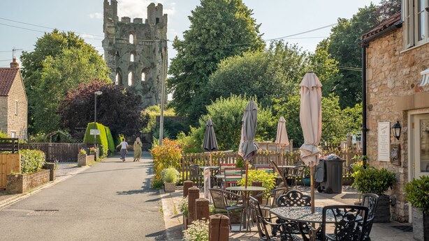 A courtyard with outdoor seating, a stone building, and a castle in the background. - Fairview, Ampleforth, North York Moors (Ampleforth)