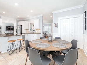 A modern kitchen with white cabinets, a central island with stools, and a dining area with a round table and chairs. - A Wave From It All by Tybee Vacation Rentals (Tybee Island)