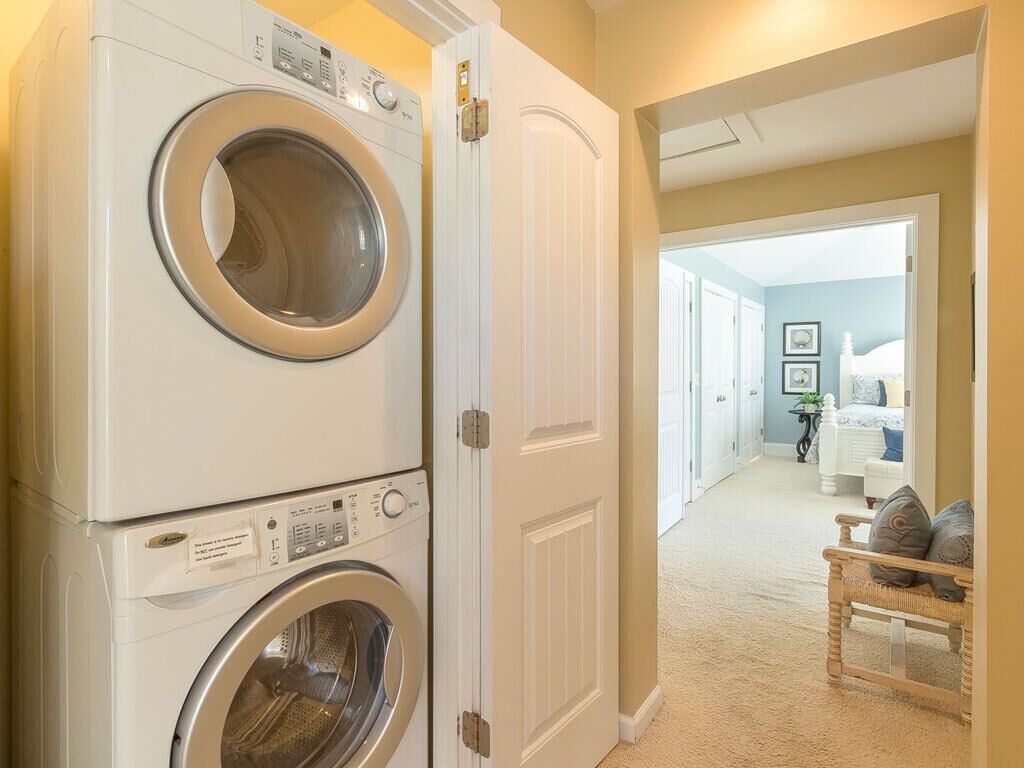 A laundry area with stacked washers and dryers, a bench with cushions, and a hallway leading to a bedroom.