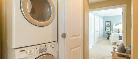 A laundry area with stacked washers and dryers, a bench with cushions, and a hallway leading to a bedroom.