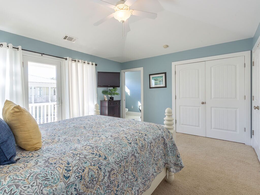 Une chambre à coucher avec un lit, un ventilateur de plafond, une porte et une fenêtre avec des rideaux.