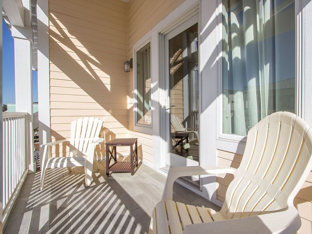 A covered porch with two Adirondack chairs and a small table, wooden siding, and a glass door leading to an interior space.