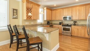Cocina con armarios de madera, encimeras de granito, una isla central con taburetes de bar, electrodomésticos de acero inoxidable e iluminación colgante.
