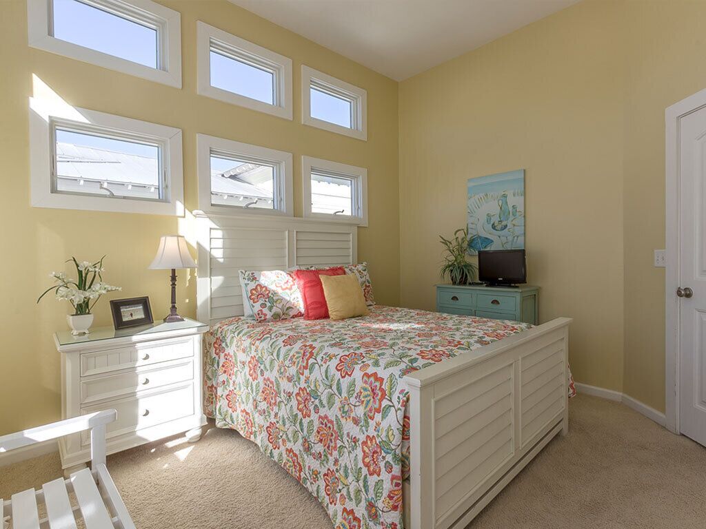A bedroom with a bed, a nightstand, a dresser, a TV, and a window with blinds.