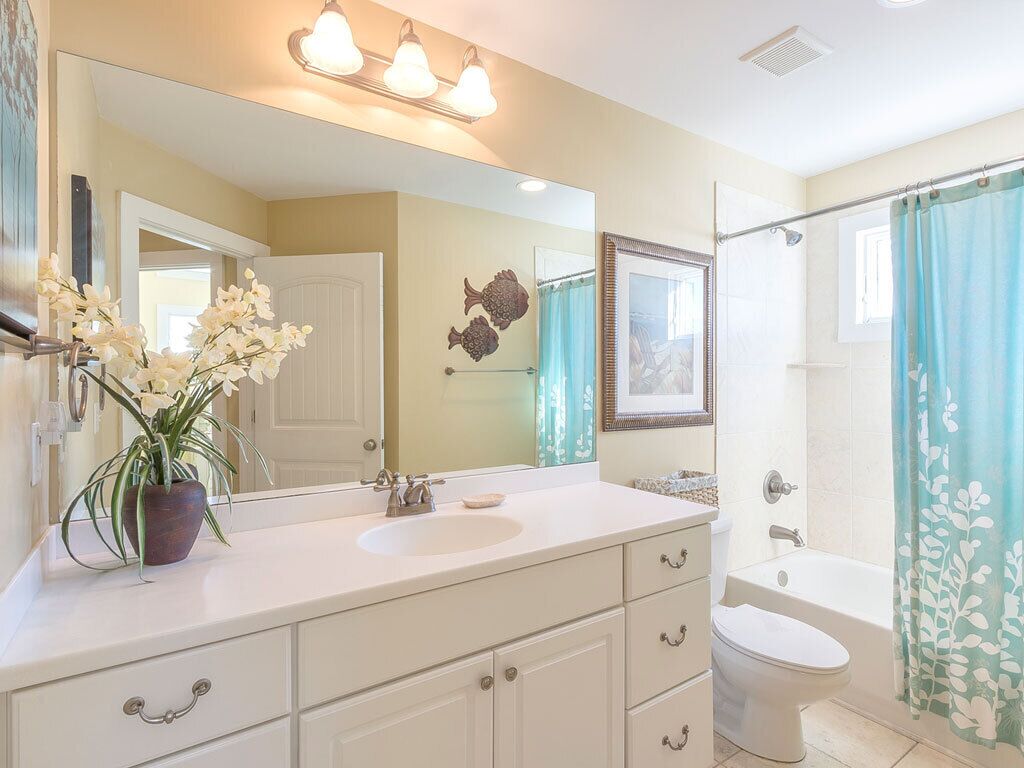 A bathroom with a white sink, mirror, and toilet. There is a shower curtain with a floral pattern.