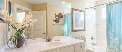 A bathroom with a white sink, mirror, and toilet. There is a shower curtain with a floral pattern.
