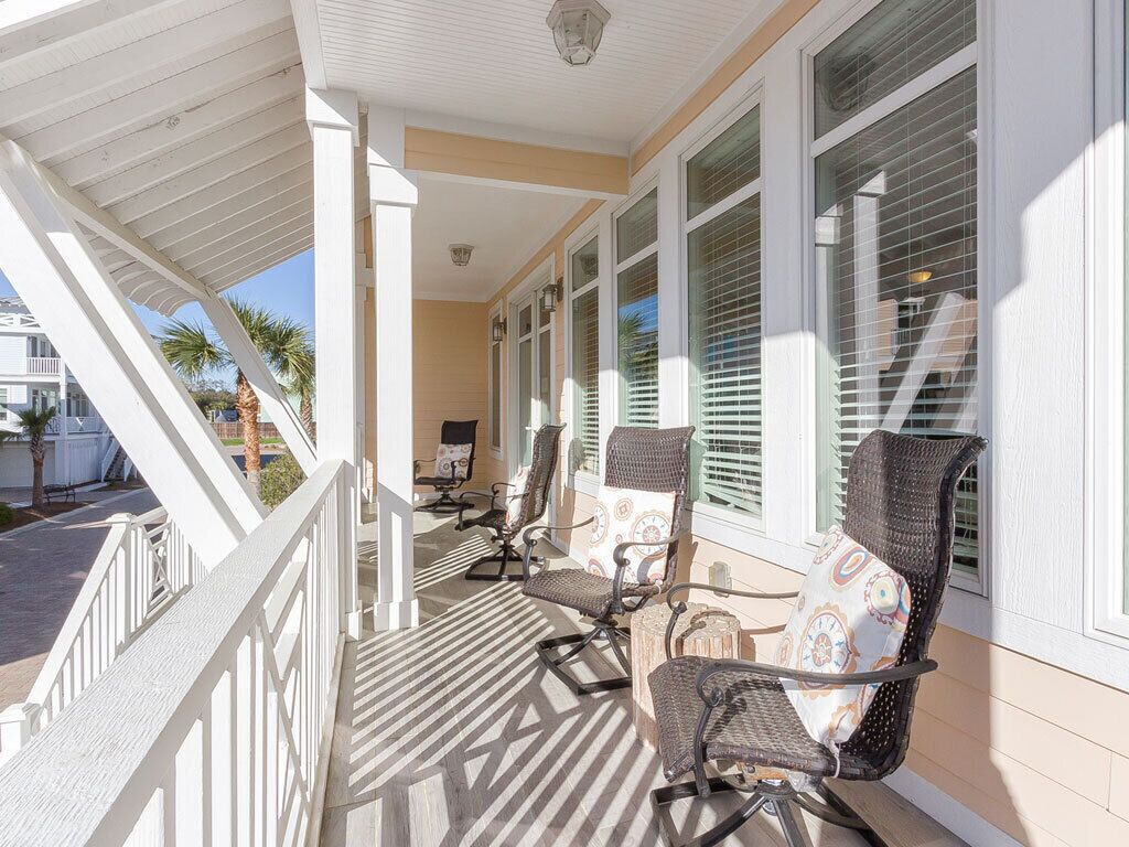 A covered porch with white railings, two rocking chairs, and a patterned cushion.