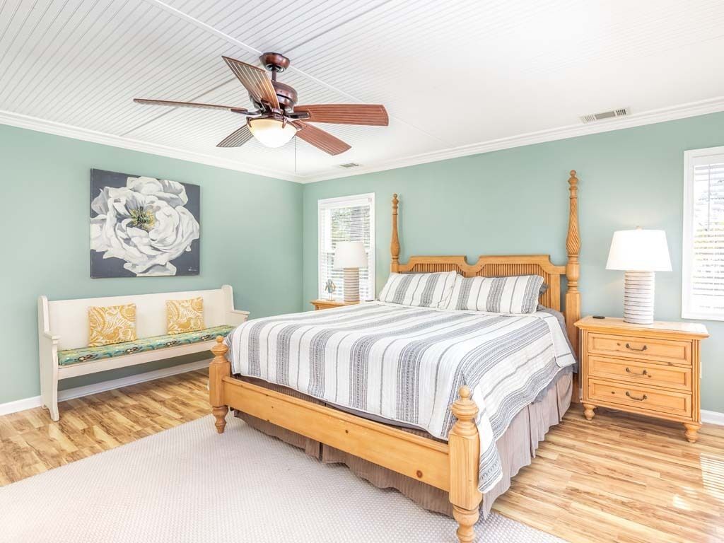 Un dormitorio con cama de madera, ventilador de techo, banco, mesita de noche y lámpara de pared.