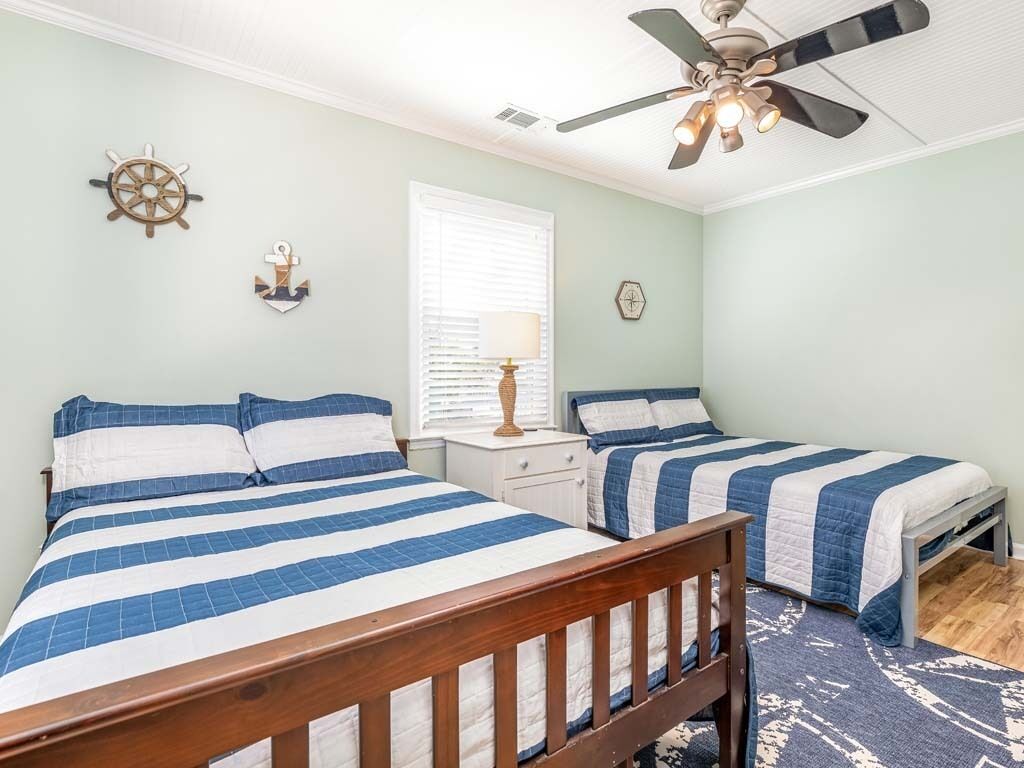 A bedroom with two beds, a ceiling fan, a window with blinds, a nightstand, and wall decorations.
