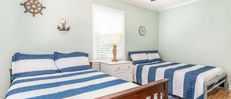 A bedroom with two beds, a ceiling fan, a window with blinds, a nightstand, and wall decorations.