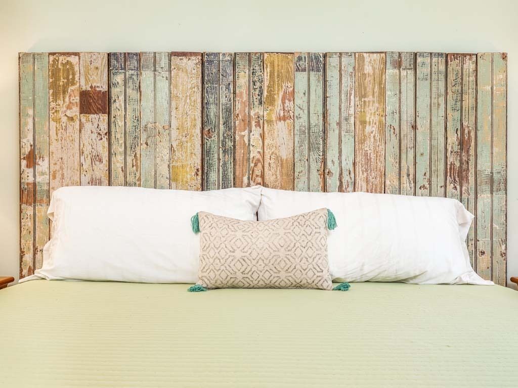 A bed with white linens and a single decorative pillow against a rustic wooden headboard.