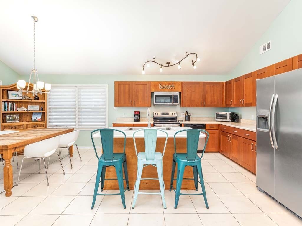 A kitchen with wooden cabinets, a stainless steel refrigerator, a dining table with chairs, and a chandelier.