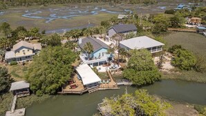 A waterfront property with multiple houses, a dock, and a large open area with water and vegetation. - All Decked Out by Tybee Vacation Rentals (Tybee Island)