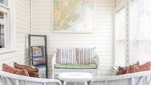 A white wicker chair with a striped cushion and a small table in a room with white walls and a map on the wall. - Annas Cabana by Tybee Vacation Rentals (Tybee Island)