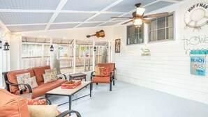 A covered patio area with a ceiling fan, a guitar, and a wall with a 'HOF MAN' sign and 'BEACH TIME' poster. - Annas Cabana by Tybee Vacation Rentals (Tybee Island)
