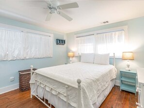 A bedroom with a white bed, two bedside lamps, a ceiling fan, and a window with curtains.