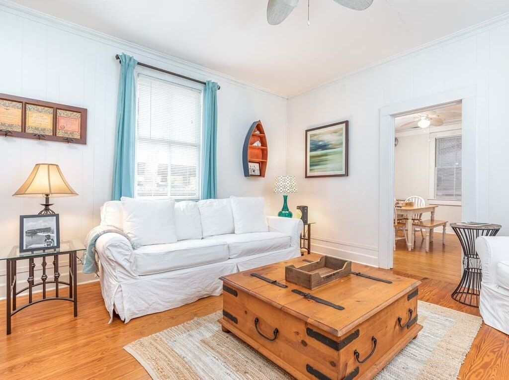 Ein Wohnzimmer mit einem weißen Sofa, einem Holztisch, einem kleinen Beistelltisch und einem gerahmten Zertifikat an der Wand.