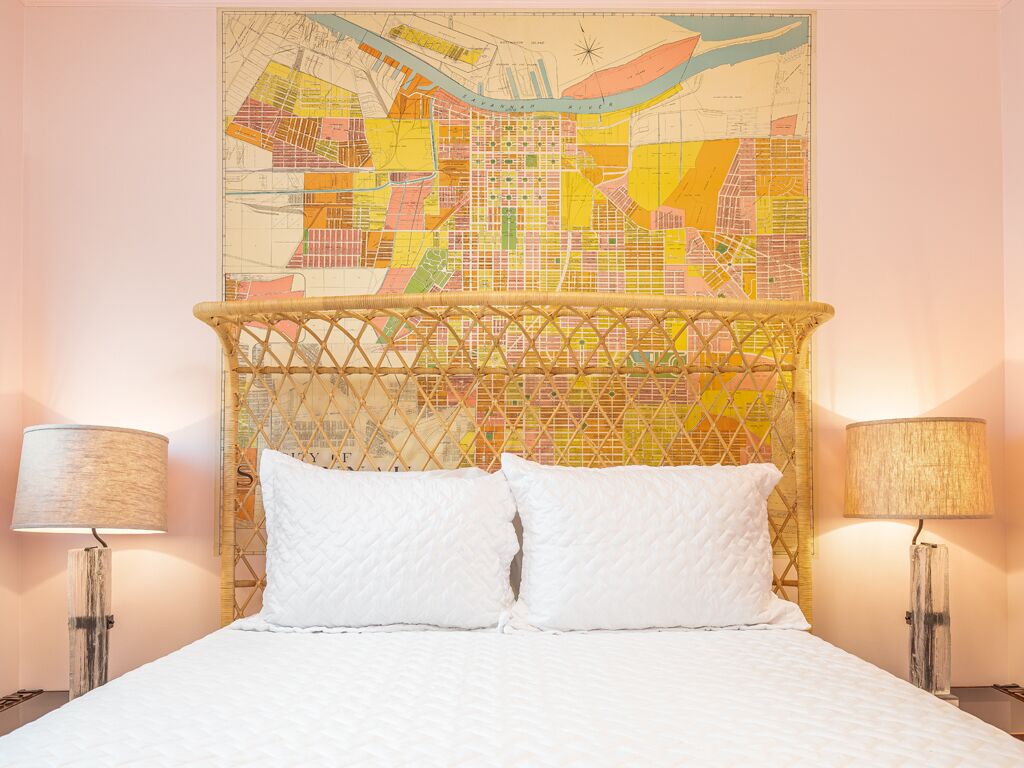 A hotel room with a bed, two bedside lamps, and a large cityscape map on the wall.