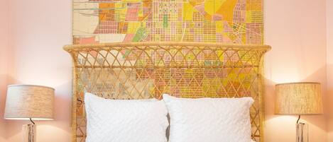 A hotel room with a bed, two bedside lamps, and a large cityscape map on the wall.
