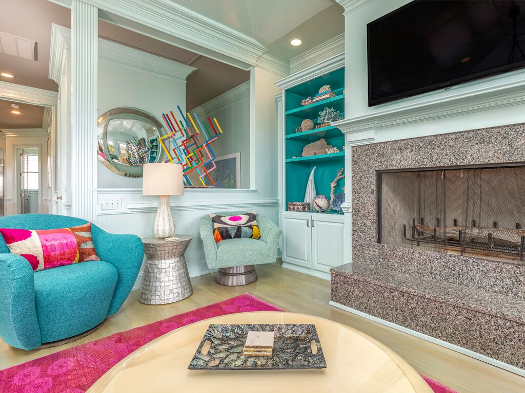 A living room with teal armchairs, a fireplace, a television, and decorative items on shelves.