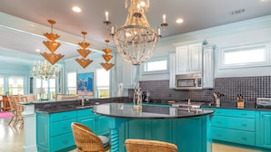 A spacious kitchen with teal cabinetry, a large island with bar stools, and a chandelier. - Aqua Vitae by Tybee Vacation Rentals (Tybee Island)