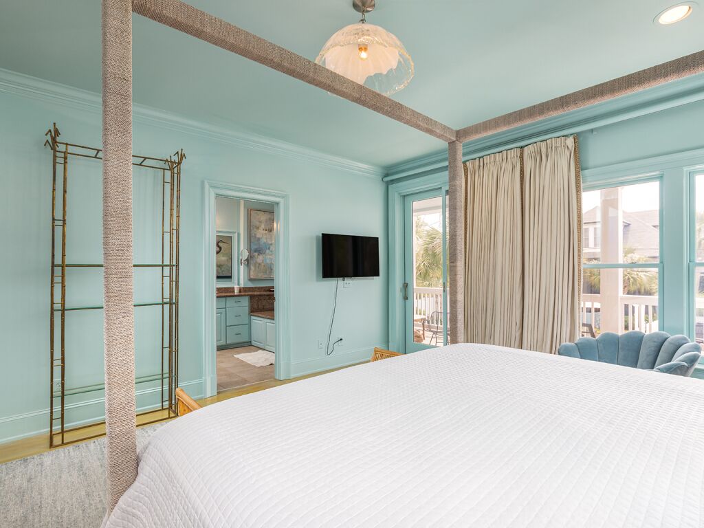 Ein Schlafzimmer mit einem großen Bett, einem Fernseher, einem Fenster mit Vorhängen und Blick ins Freie.