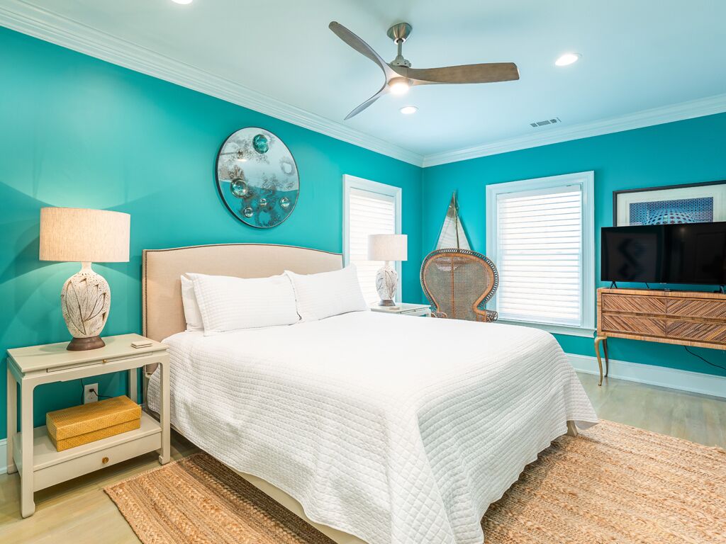 A bedroom with a bed, nightstands, a ceiling fan, a TV, and a wall with a decorative mirror.