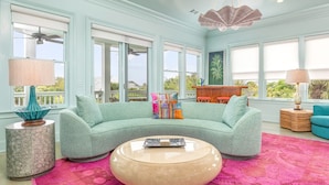 A spacious living room with a curved sofa, a round coffee table, and a vibrant pink rug. - Aqua Vitae by Tybee Vacation Rentals (Tybee Island)