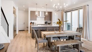 Een moderne keuken met houten kastjes, een centraal eiland, hanglampen en een eethoek met een houten tafel en stoelen.